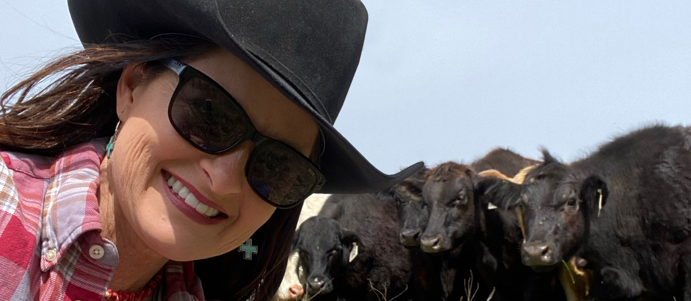 Women wearing black cowboy hat posing with cattle.